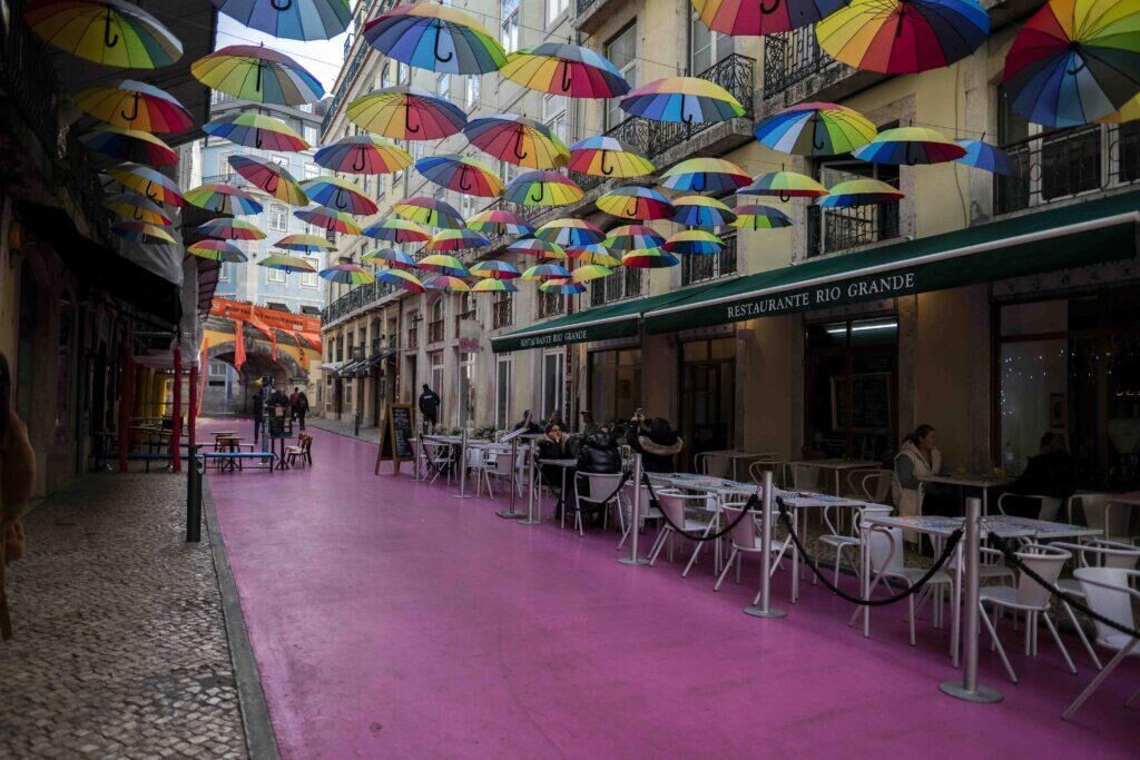 a street painted pink that's got colourful umbrellas hanging from above in Lisbon, Portugal